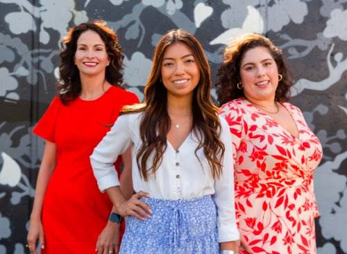3 women standing together in front of a wall