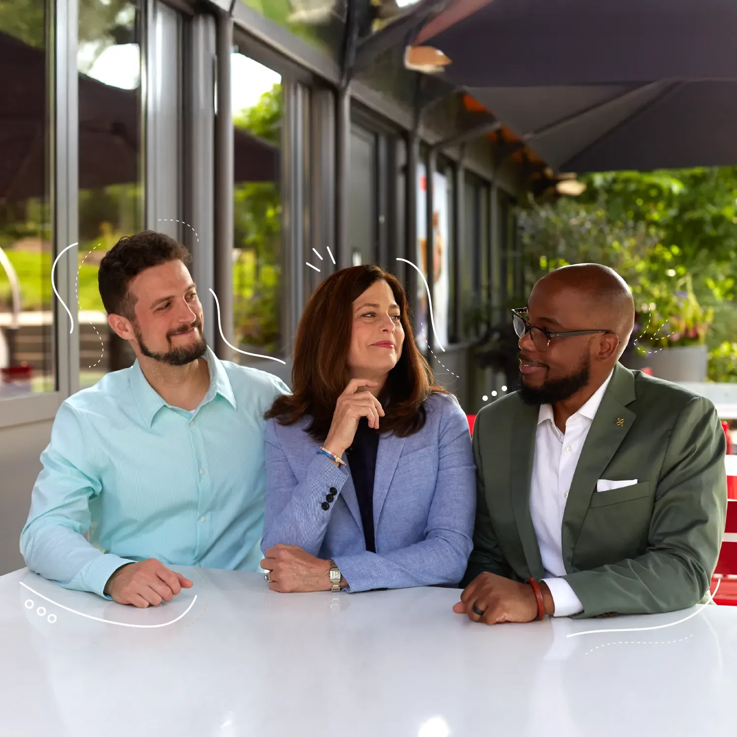 3 people sitting in a row on the patio of a cafe looking at each other with smiles surrounded by doodles